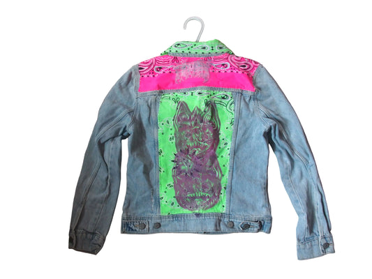 A light blue denim jacket with a white hanger, featuring a bright pink bandana pattern across the shoulders and a large purple bat graphic on a neon green background on the back.