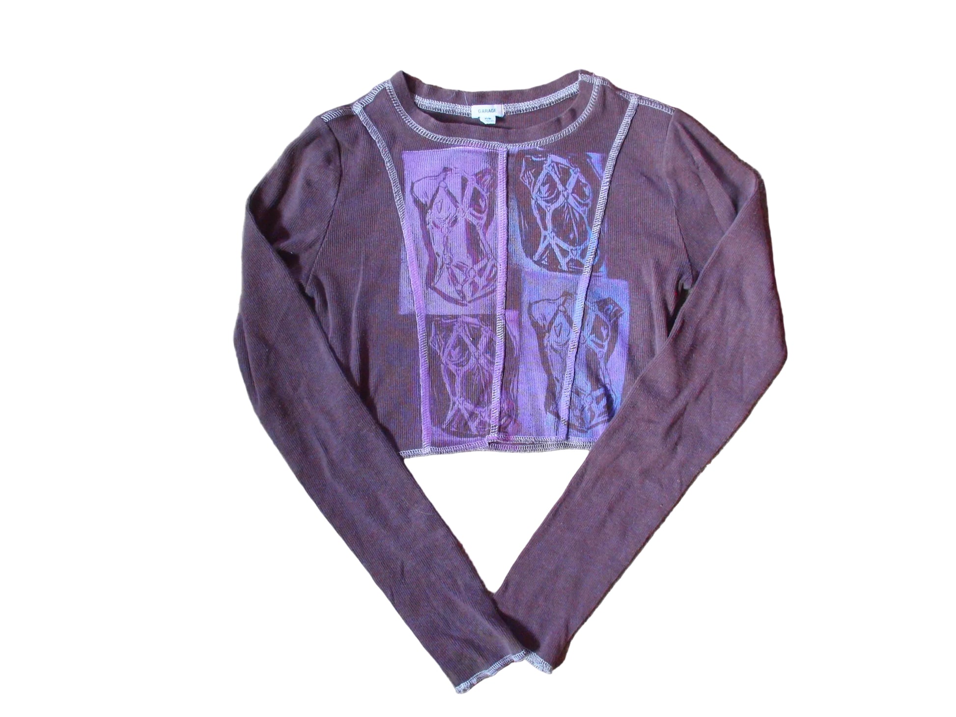 A long-sleeve cropped top in a dusty mauve-purple color, featuring a large lavender graphic print on the front with geometric and abstract patterns, laid flat on a beige carpet.